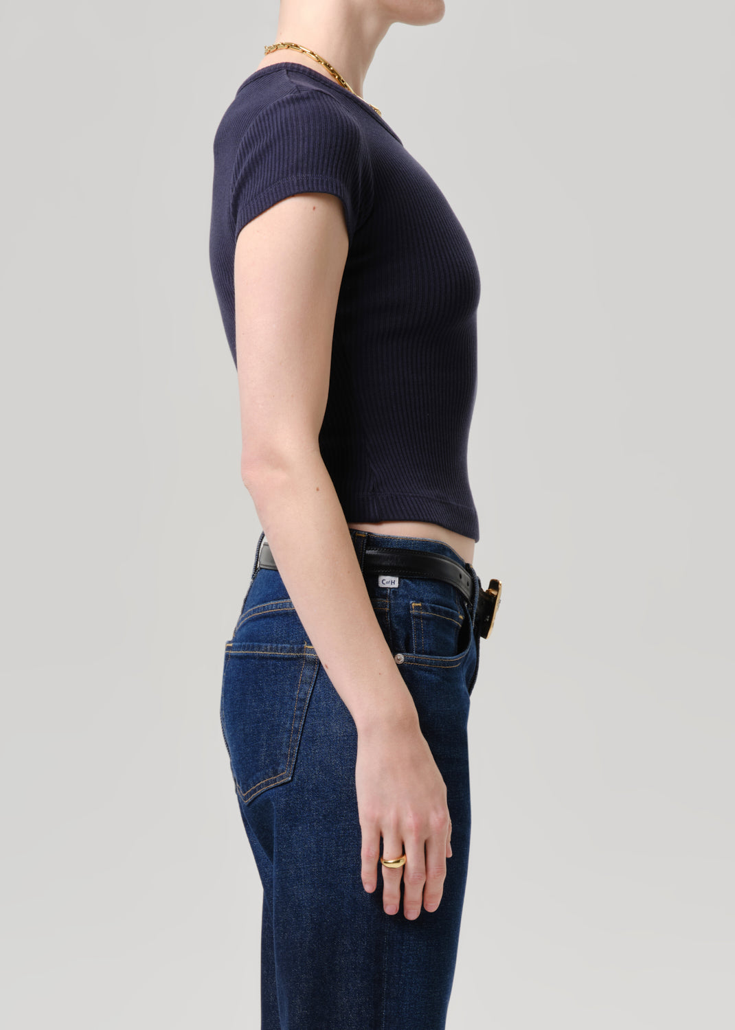 Side profile of a model wearing a dark navy ribbed short-sleeve crop top and dark blue jeans against a grey background.