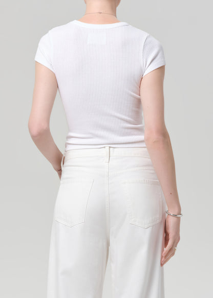 Person wearing a white ribbed t-shirt and white pants on a gray background