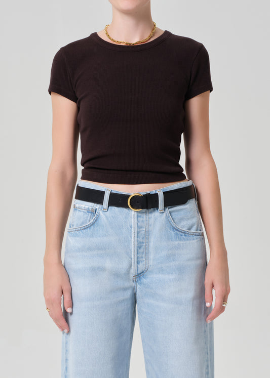 Person wearing a brown tee and light blue jeans with a black belt on a plain background