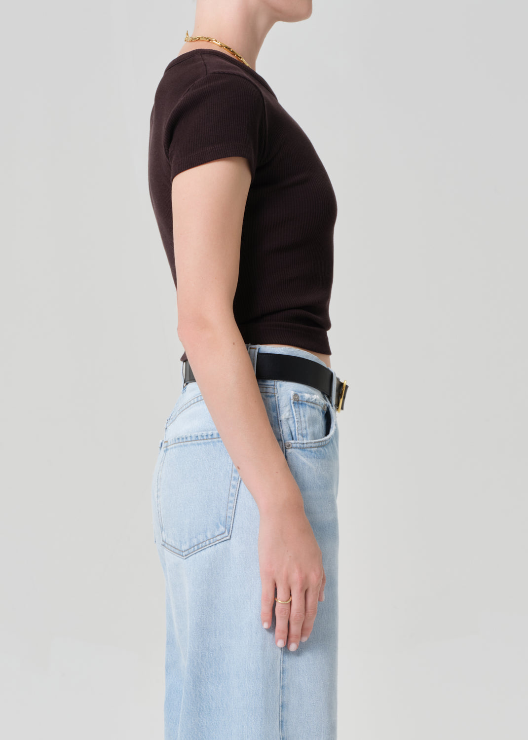 Person wearing a brown tee and light blue jeans with a black belt on a plain background