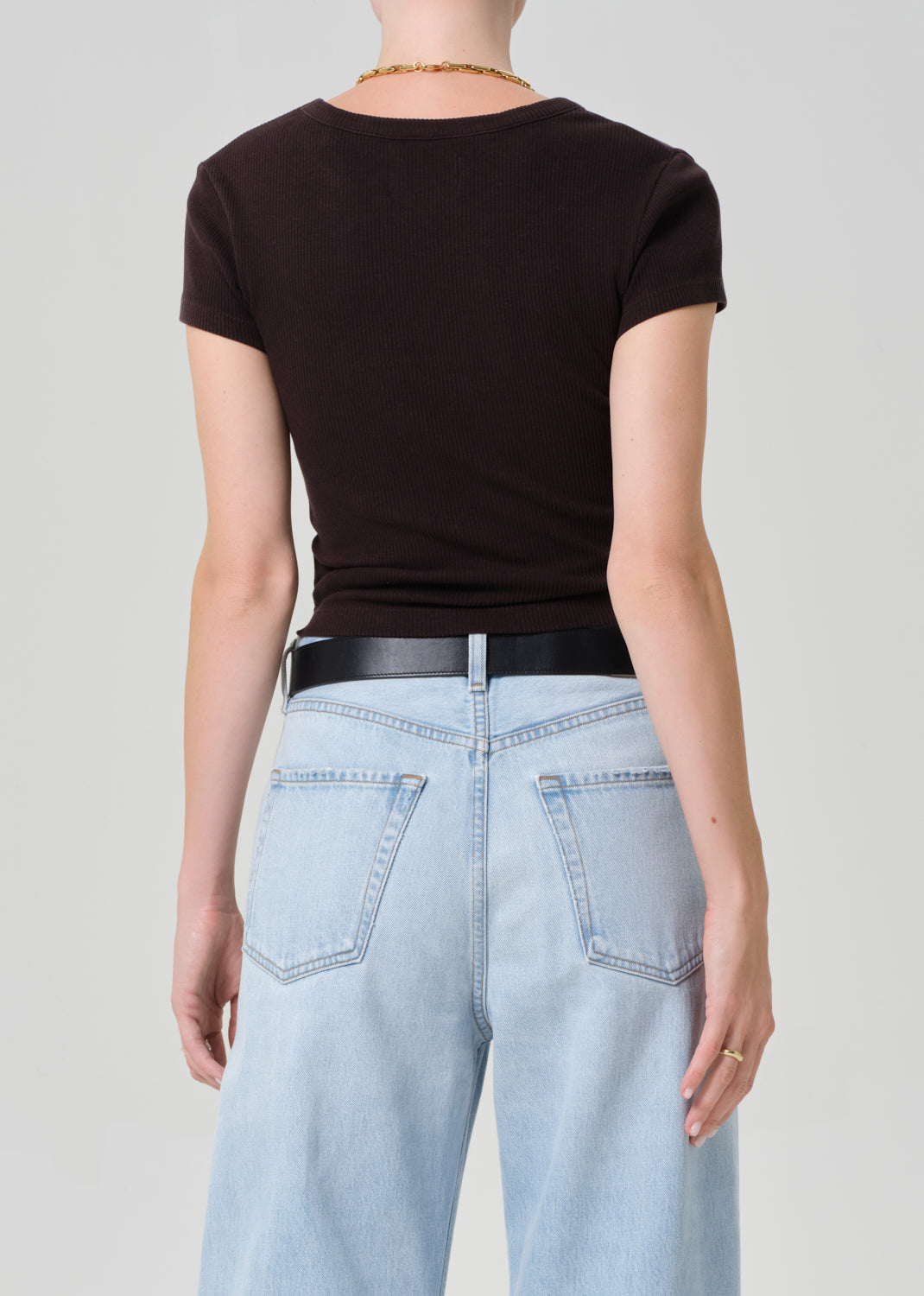 Person wearing a brown tee and light blue jeans with a black belt on a plain background