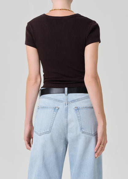 Person wearing a brown tee and light blue jeans with a black belt on a plain background