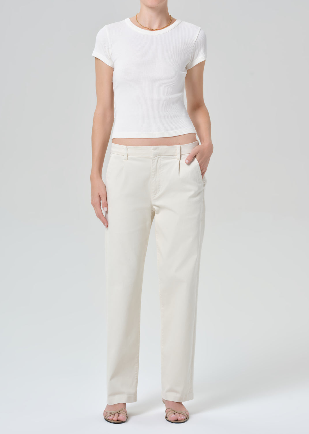 Person wearing a white crop top and beige pants on a plain background