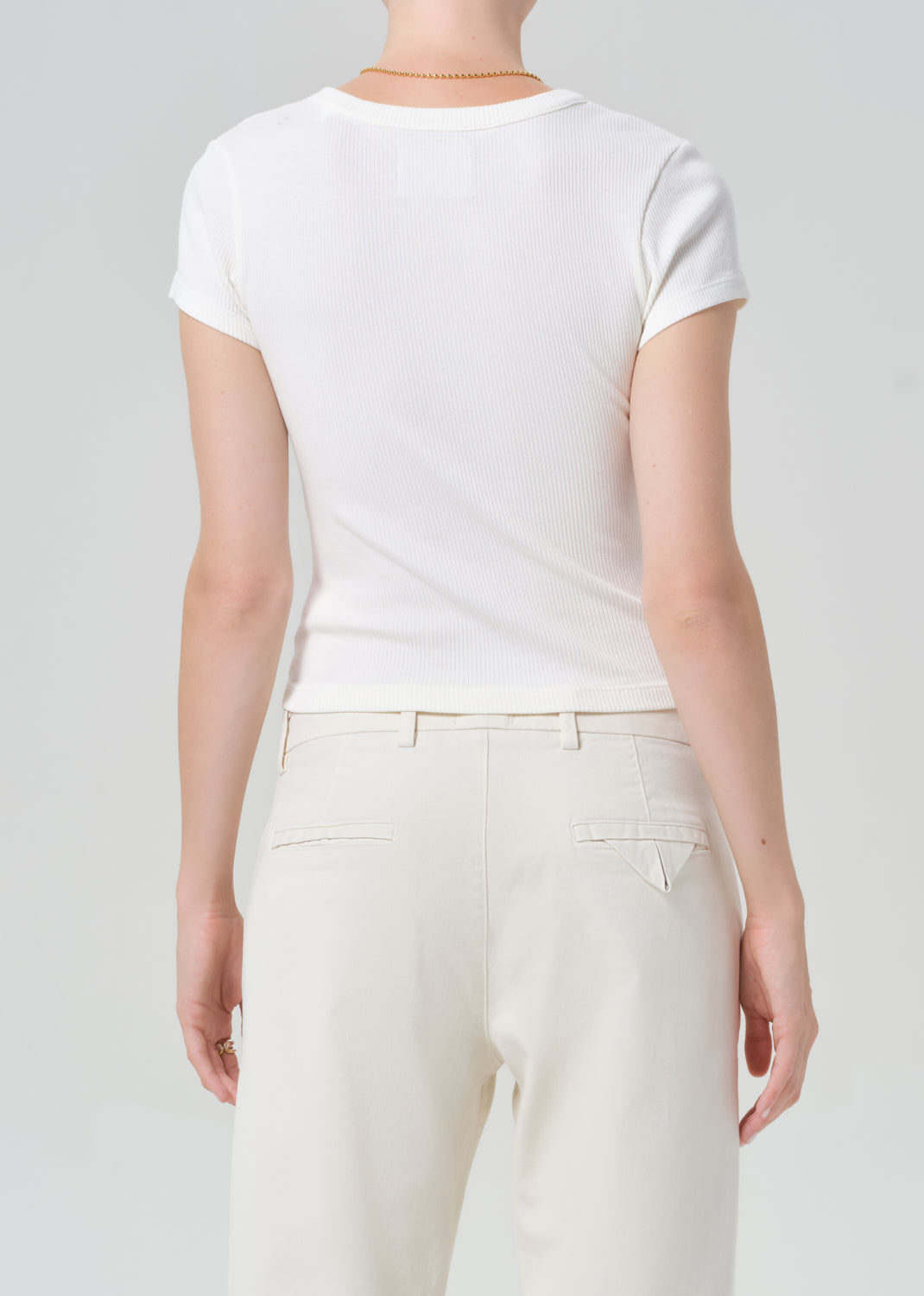 Person wearing a plain white t-shirt and light-colored pants on a neutral background