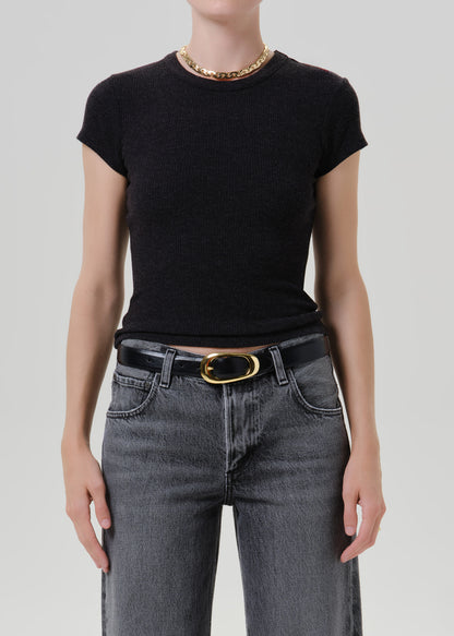 A model wearing a black short-sleeve crewneck knit top tucked into dark grey jeans with a black belt and gold buckle, accessorized with a chunky gold chain necklace, against a grey background.
