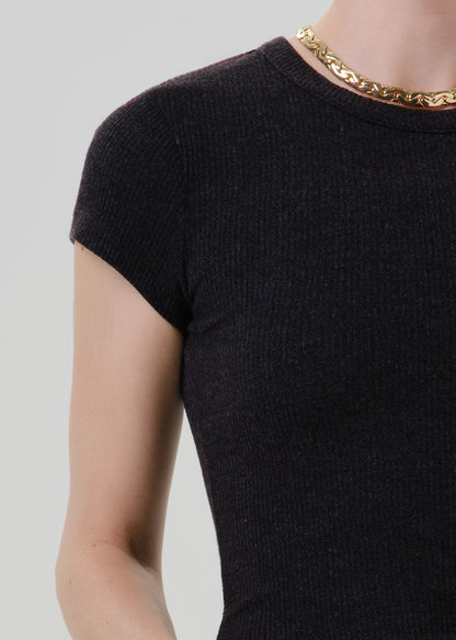 Close-up of a person wearing a dark charcoal ribbed short-sleeve top with a chunky gold chain necklace, against a grey background.