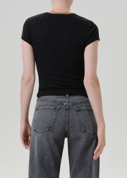 Rear view of a person wearing a fitted black short-sleeve t-shirt and dark grey jeans against a light grey studio background.