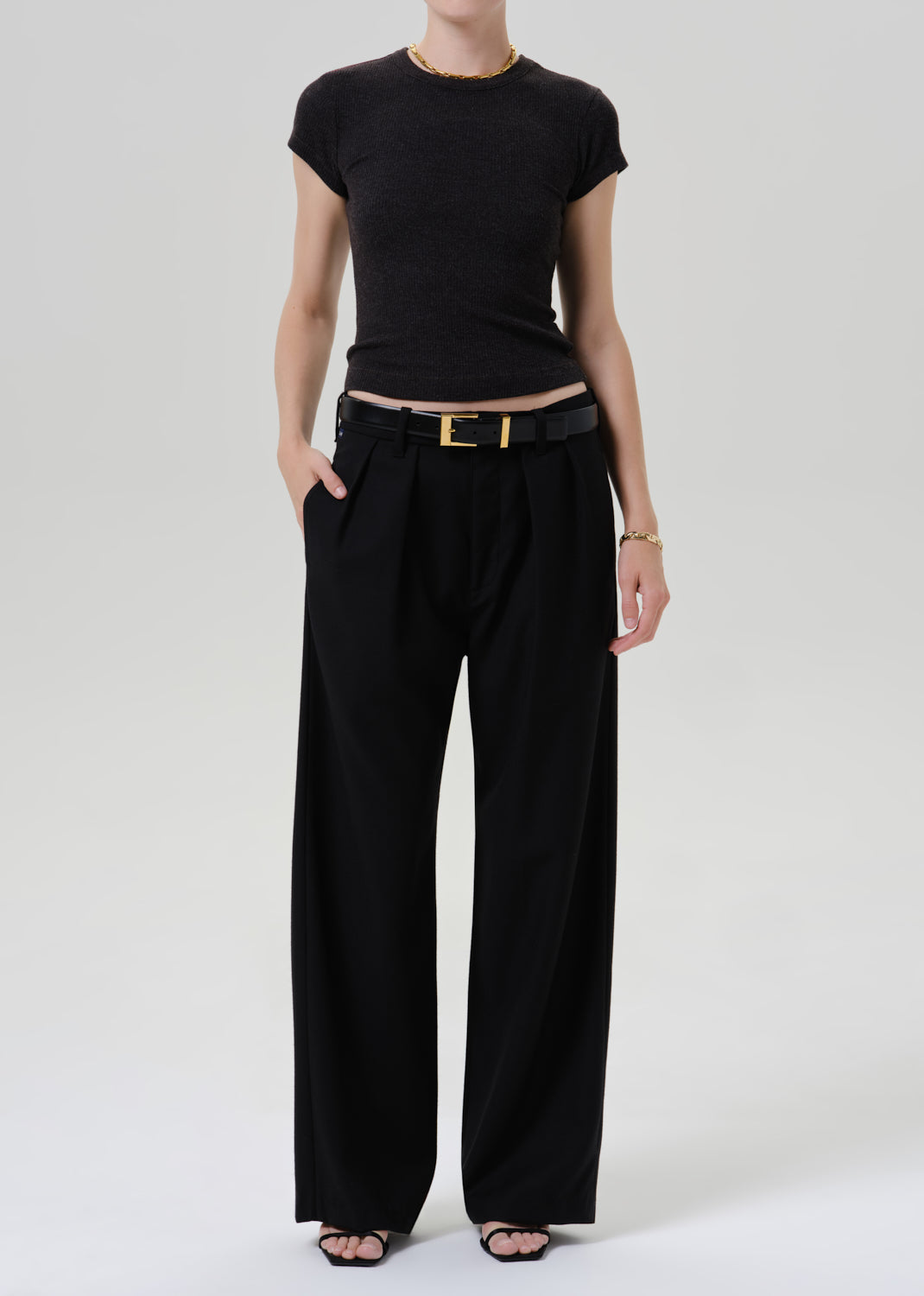 Person wearing a black ribbed cap sleeve tee with black wide leg trousers on a grey background