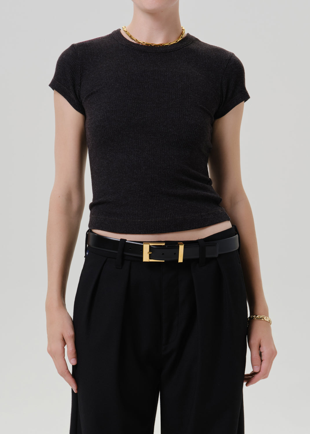 Person wearing a black ribbed cap sleeve tee on a grey background