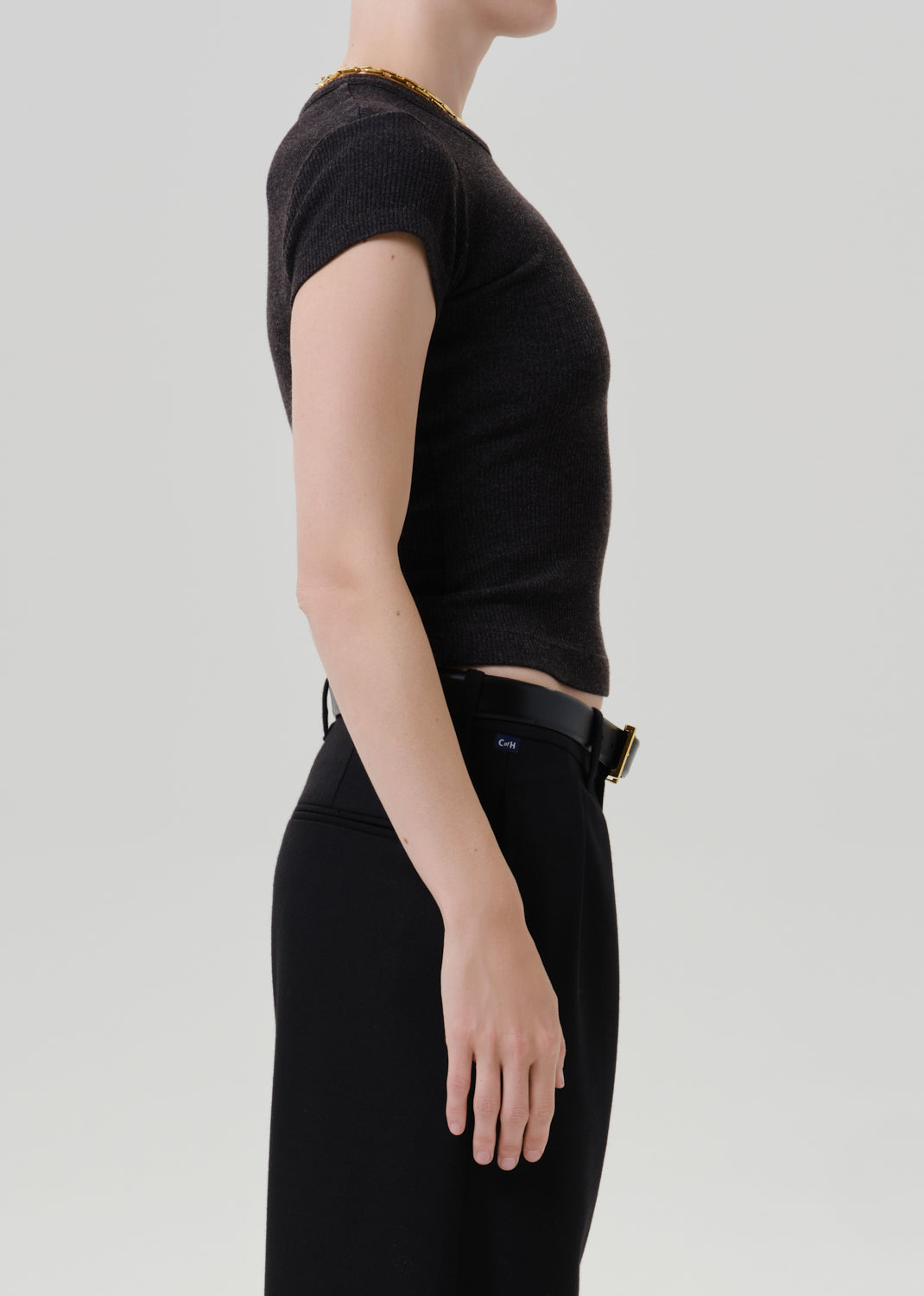 Person wearing a black ribbed cap sleeve tee with black wide leg trousers viewed from the side on a grey background