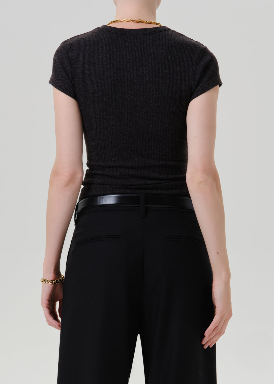 Person wearing a black ribbed cap sleeve tee with black wide leg trousers viewed from the back on a grey background