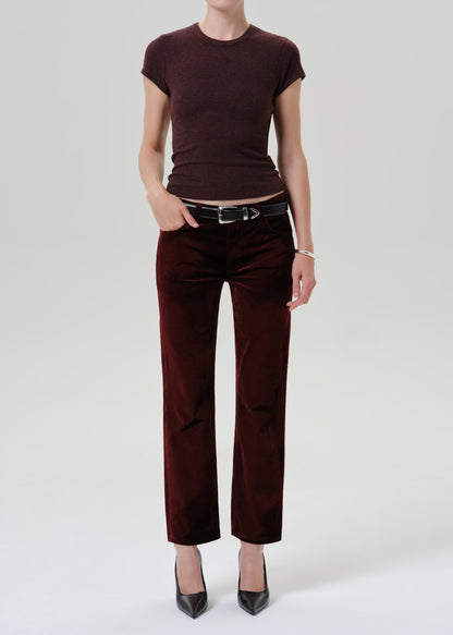 A model wearing a dark burgundy short-sleeve knit top and matching wide-leg trousers in a velvet-like fabric, styled with a black belt and black pointed-toe heels against a grey background.