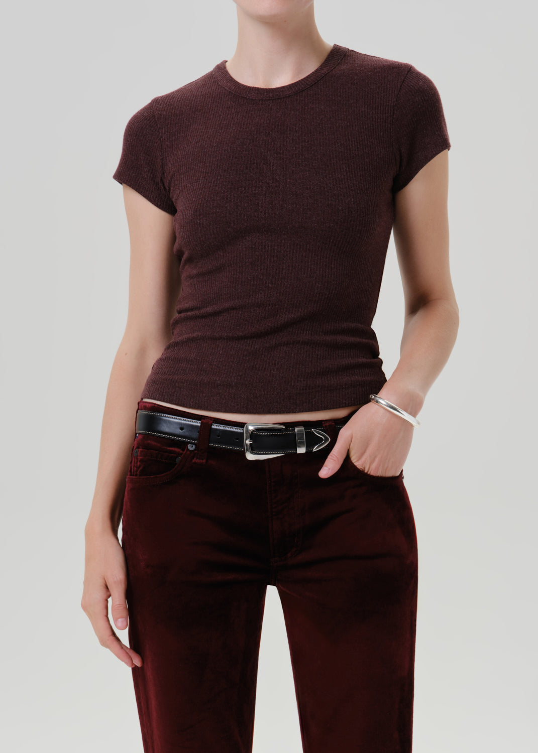 A model wearing a short-sleeve crewneck knit top in a deep burgundy color, paired with burgundy pants and a black belt, against a grey background.