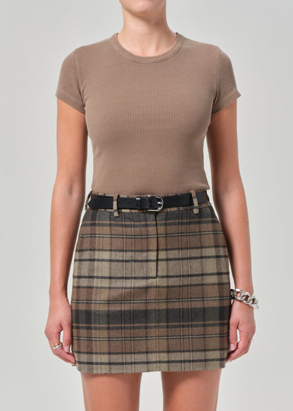Person wearing a brown ribbed t-shirt and plaid skirt on a plain background