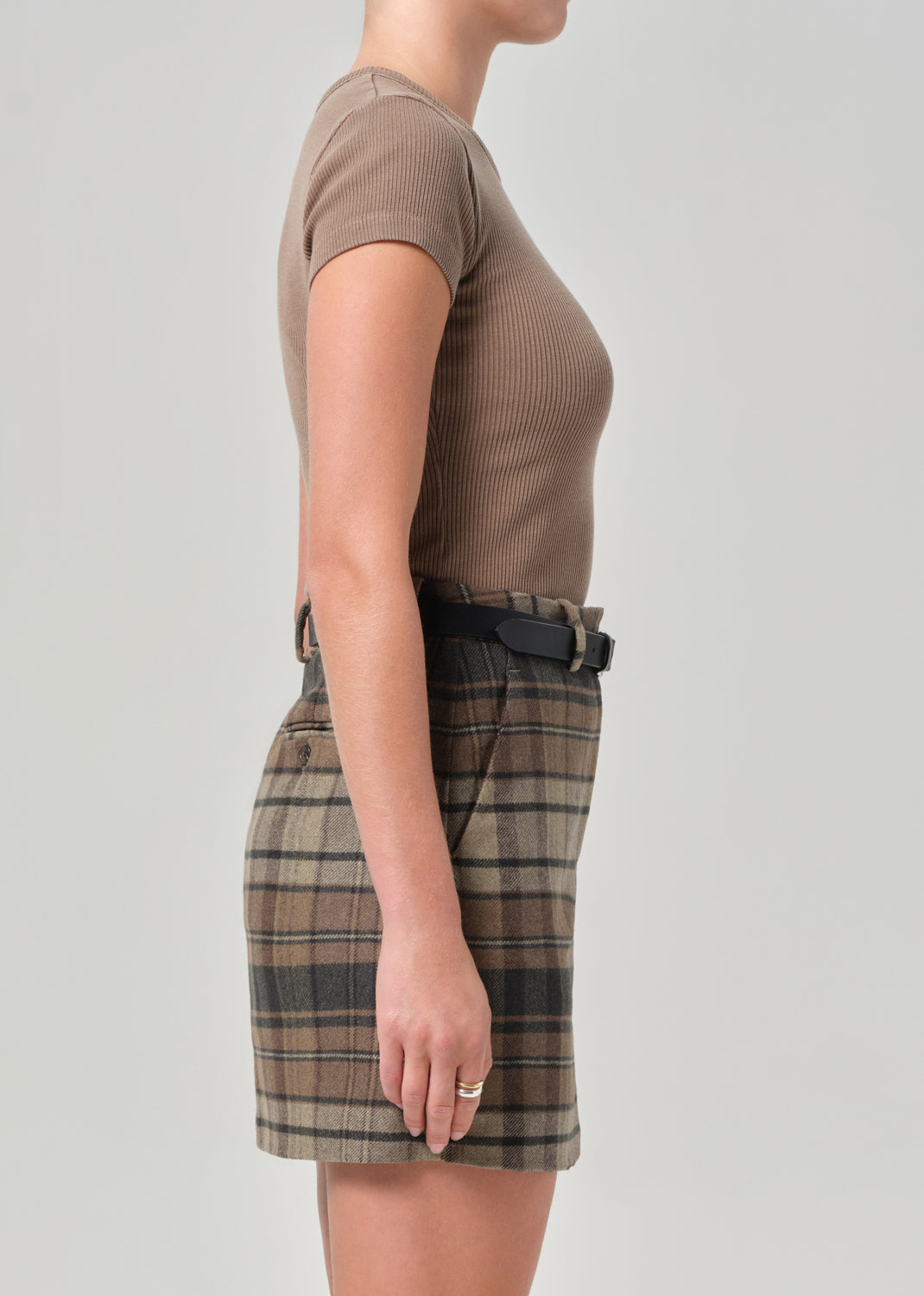 Person wearing a brown ribbed t-shirt and plaid skirt on a plain background