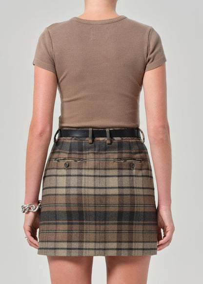 Person wearing a brown ribbed top and plaid skirt on a plain background