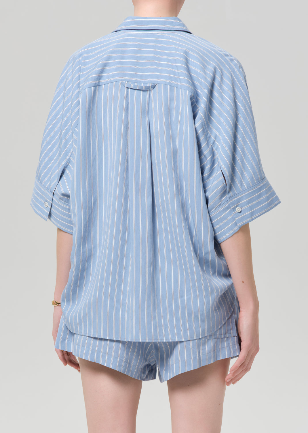 Person wearing a blue striped shirt and matching shorts on a grey background