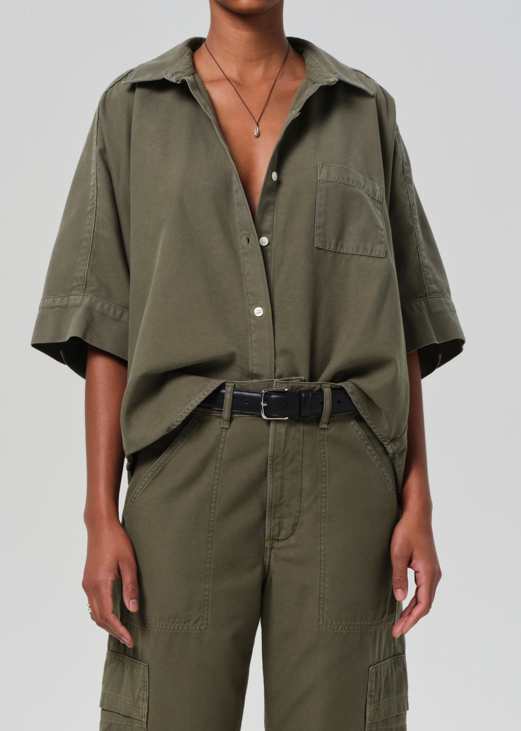 Person wearing an olive green outfit with a matching shirt and pants on a white background