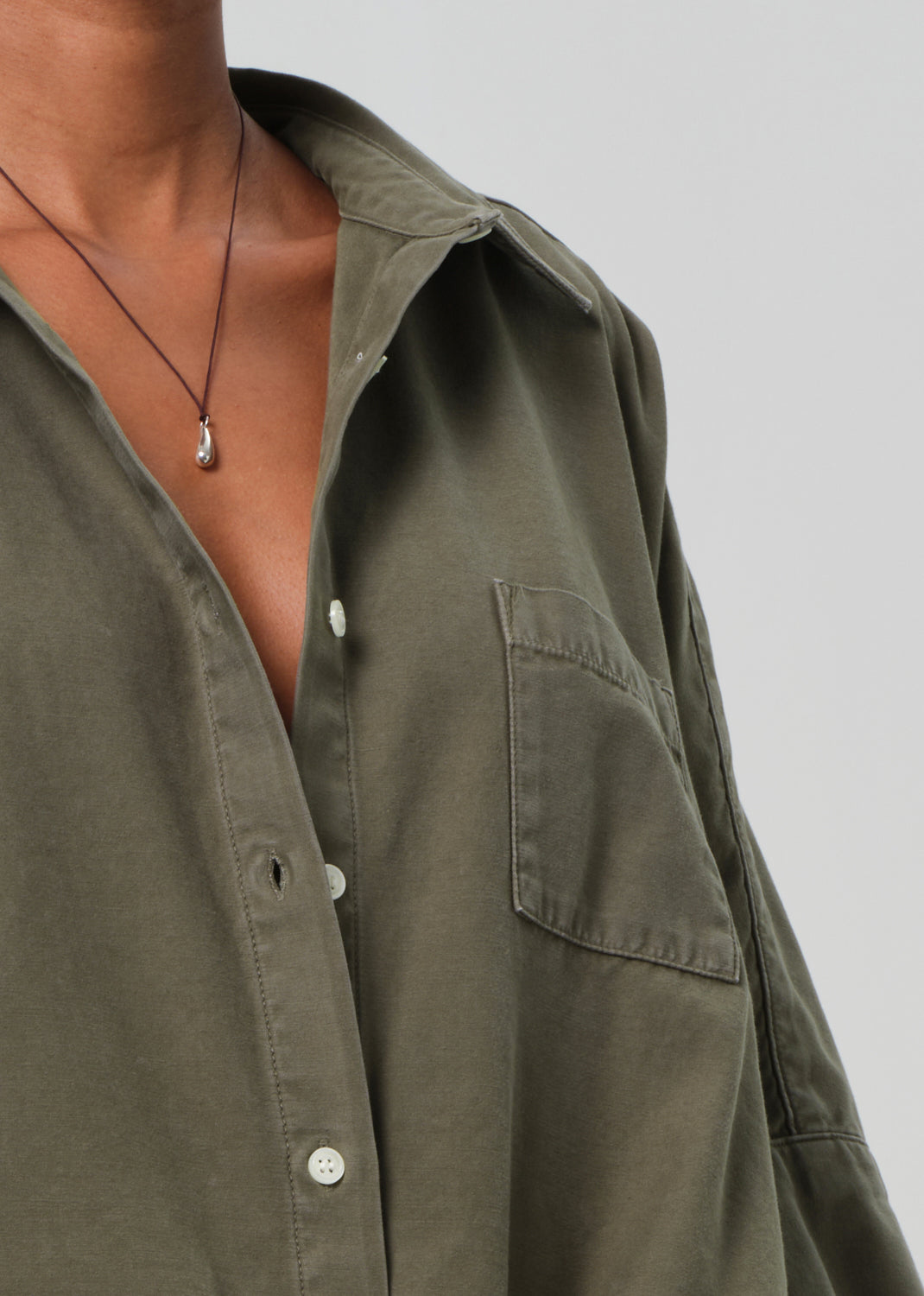 Close-up of a person wearing an olive green shirt with a necklace on a plain background