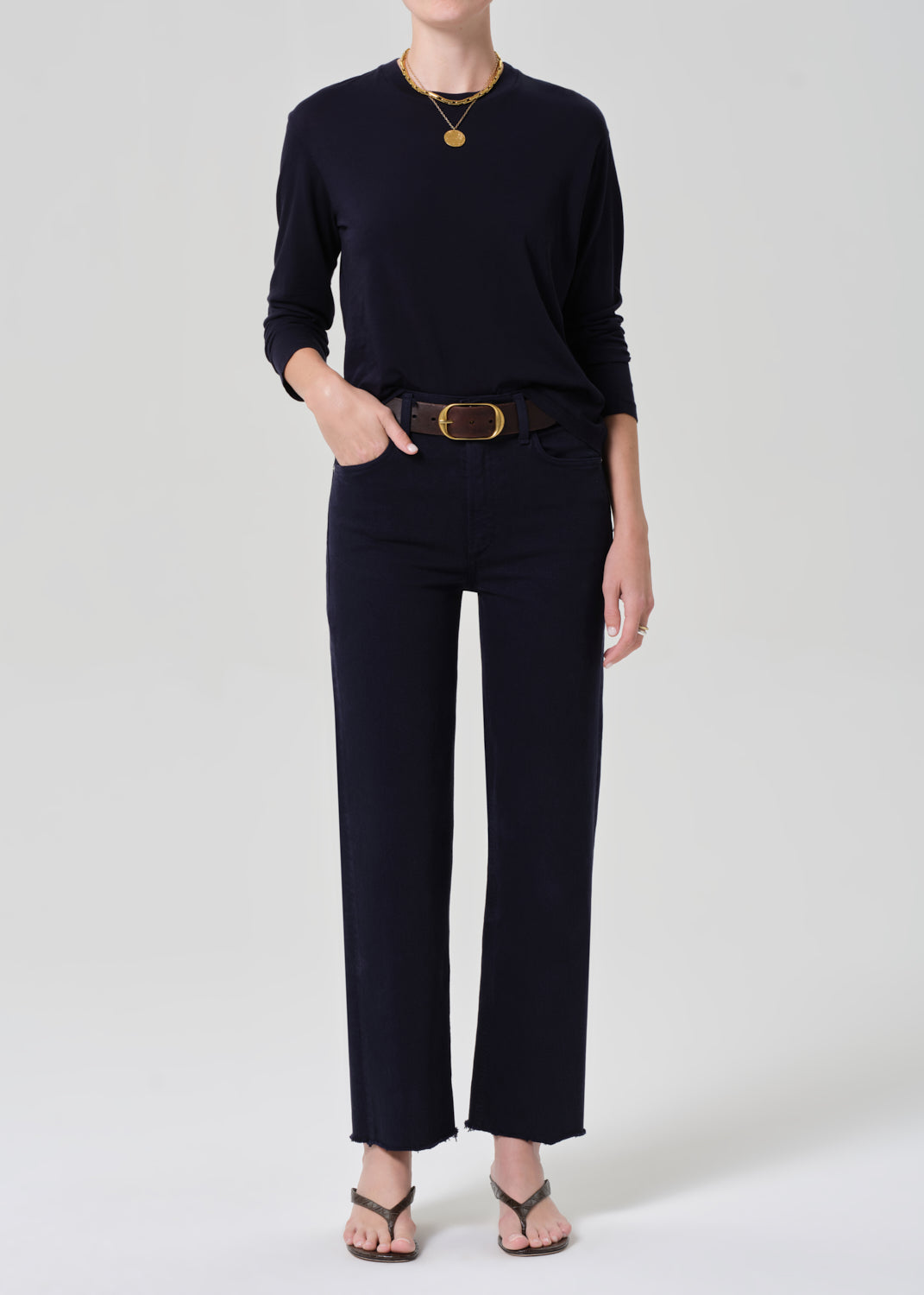 Person wearing a navy shirt and dark pants with a belt on a light gray background