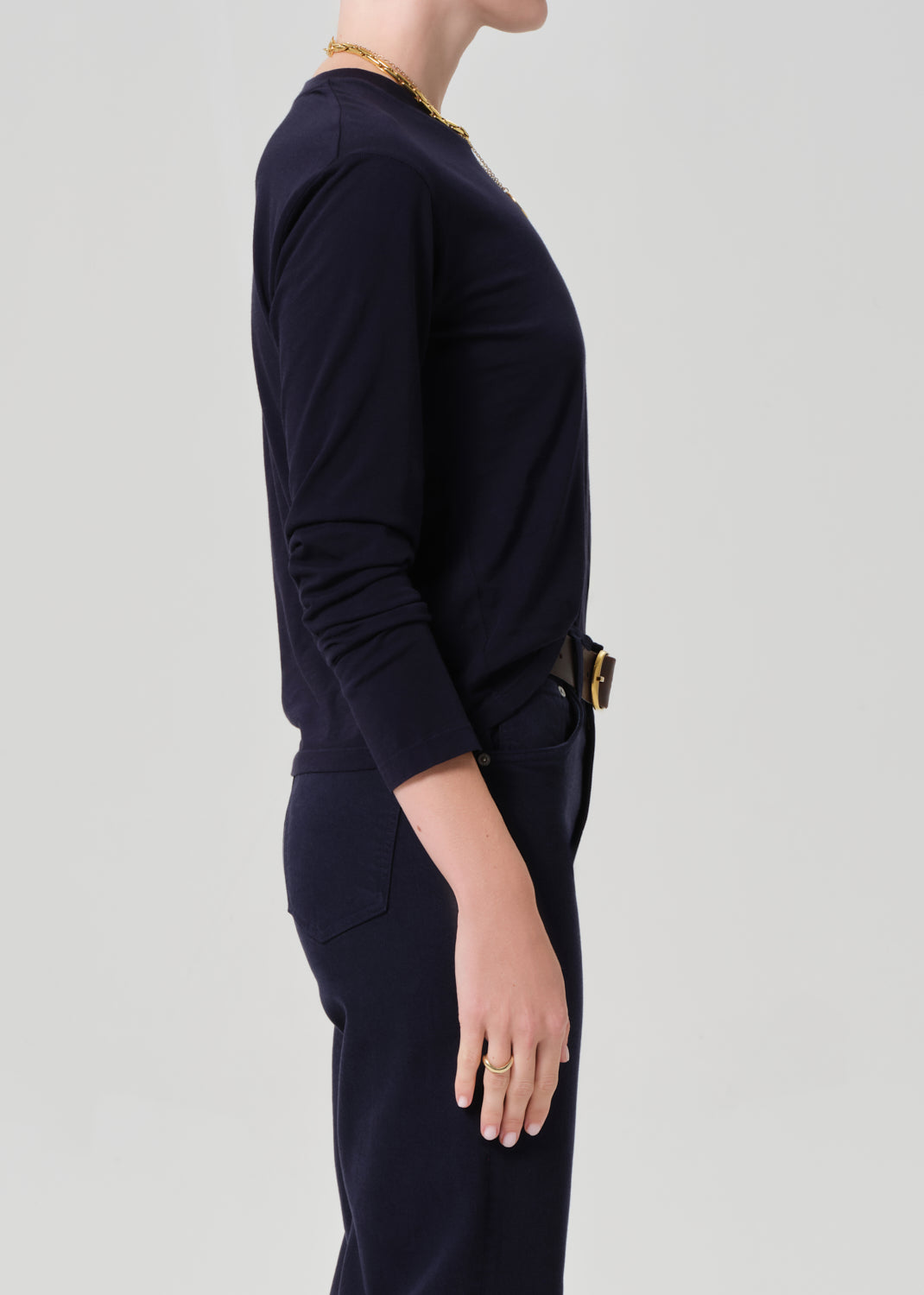 Person wearing a navy shirt and dark pants with a belt on a light gray background