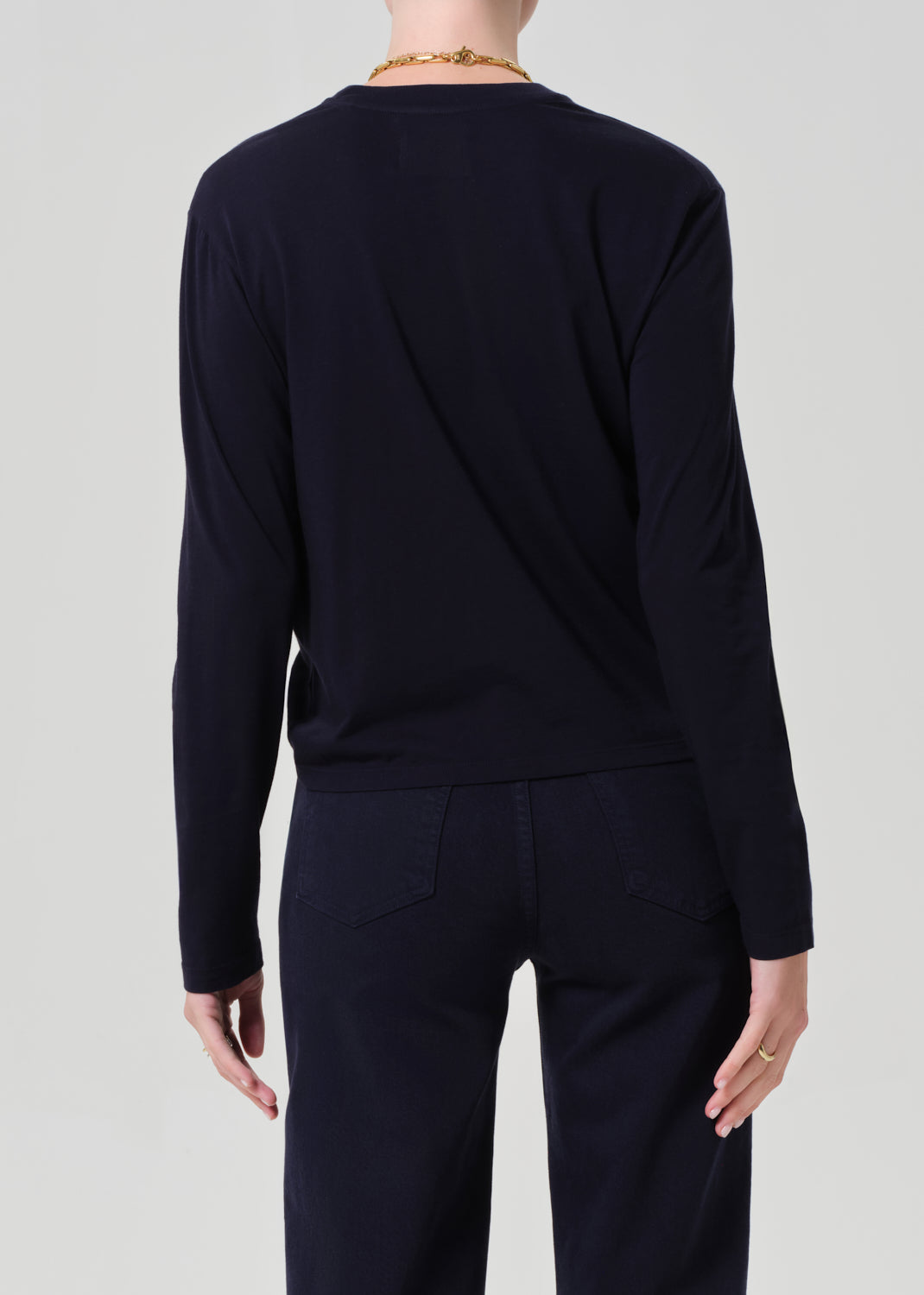 Person wearing a navy shirt and dark pants with a belt on a light gray background