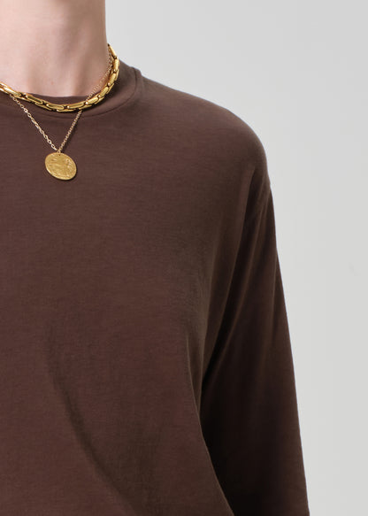 Person wearing a brown long-sleeve shirt with gold necklaces on a light gray background