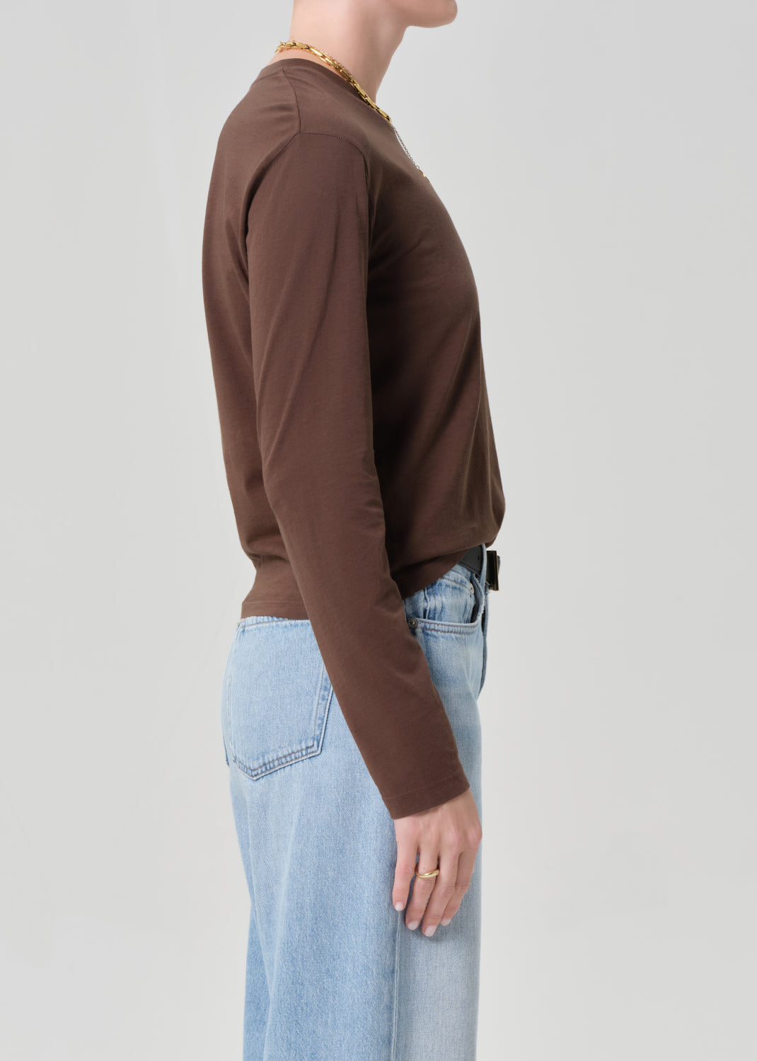 Person wearing a brown long-sleeve top and light blue jeans on a plain background