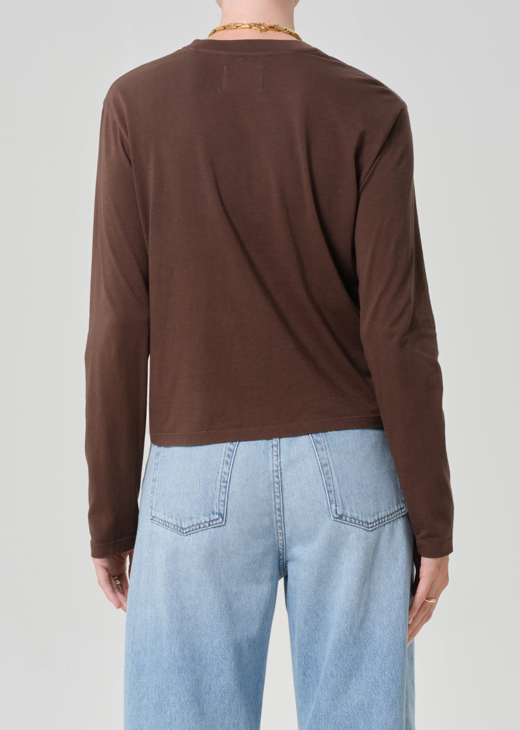 Person wearing a brown long-sleeve shirt and light blue jeans on a plain background