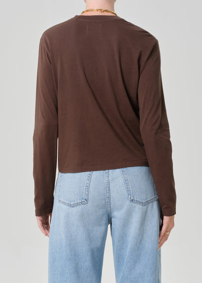 Person wearing a brown long-sleeve shirt and light blue jeans on a plain background