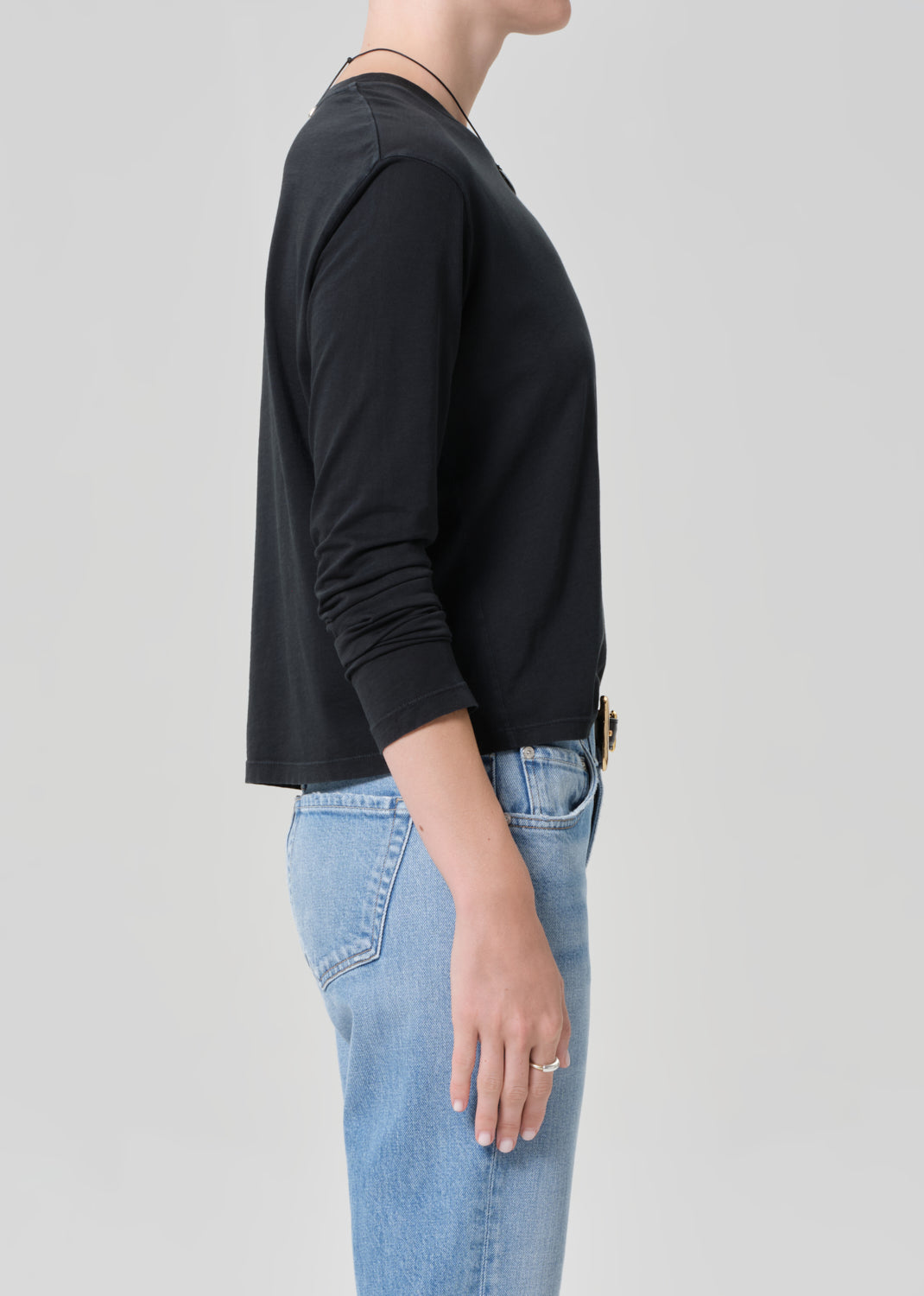 Person wearing a black long-sleeve shirt and blue jeans on a light gray background