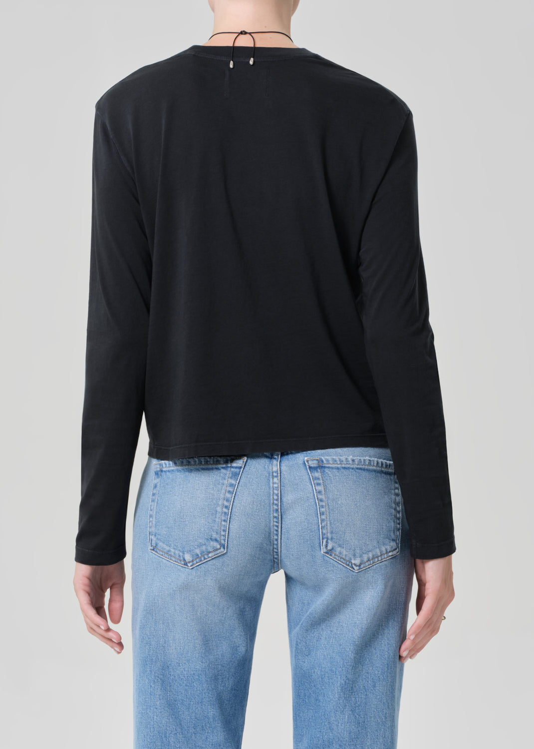 Person wearing a black long-sleeve shirt and light blue jeans on a plain background