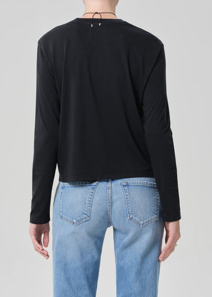 Person wearing a black long-sleeve shirt and light blue jeans on a plain background