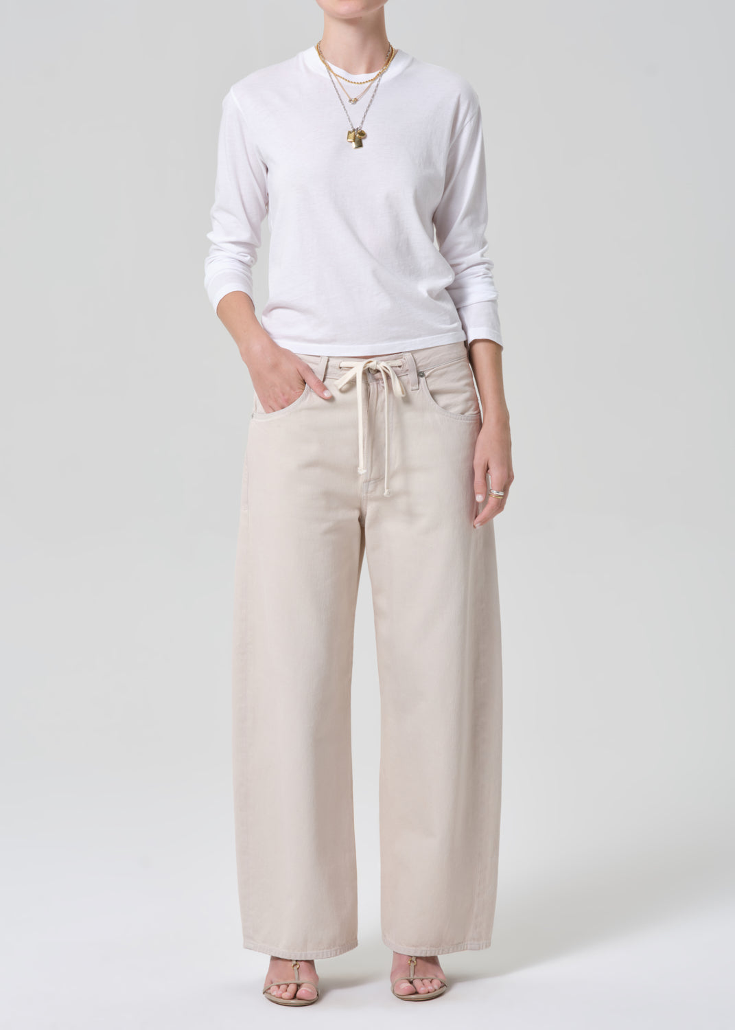 Person wearing a white long-sleeve shirt and beige wide-leg pants on a plain background