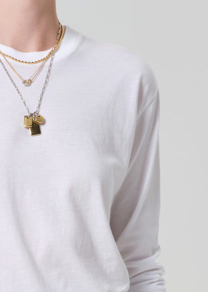 Person wearing a white long-sleeve shirt with gold necklaces on a plain background