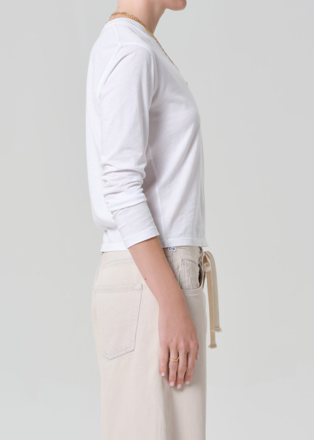 Person wearing a white long-sleeve shirt and beige pants on a plain background