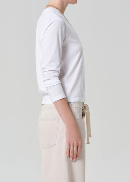 Person wearing a white long-sleeve shirt and beige pants on a plain background