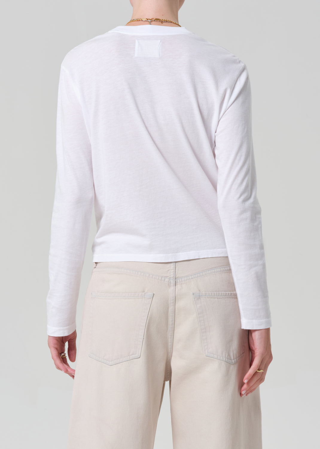 Person wearing a white long-sleeve shirt and beige pants on a plain background