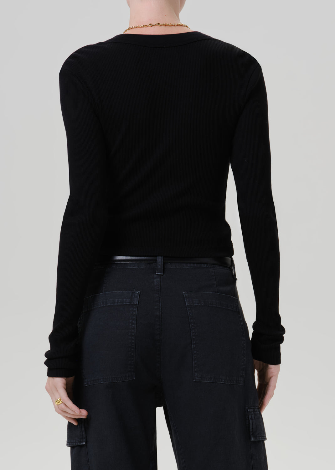 A person shown from the back wearing a fitted black long-sleeve top and dark cargo-style pants against a grey background.