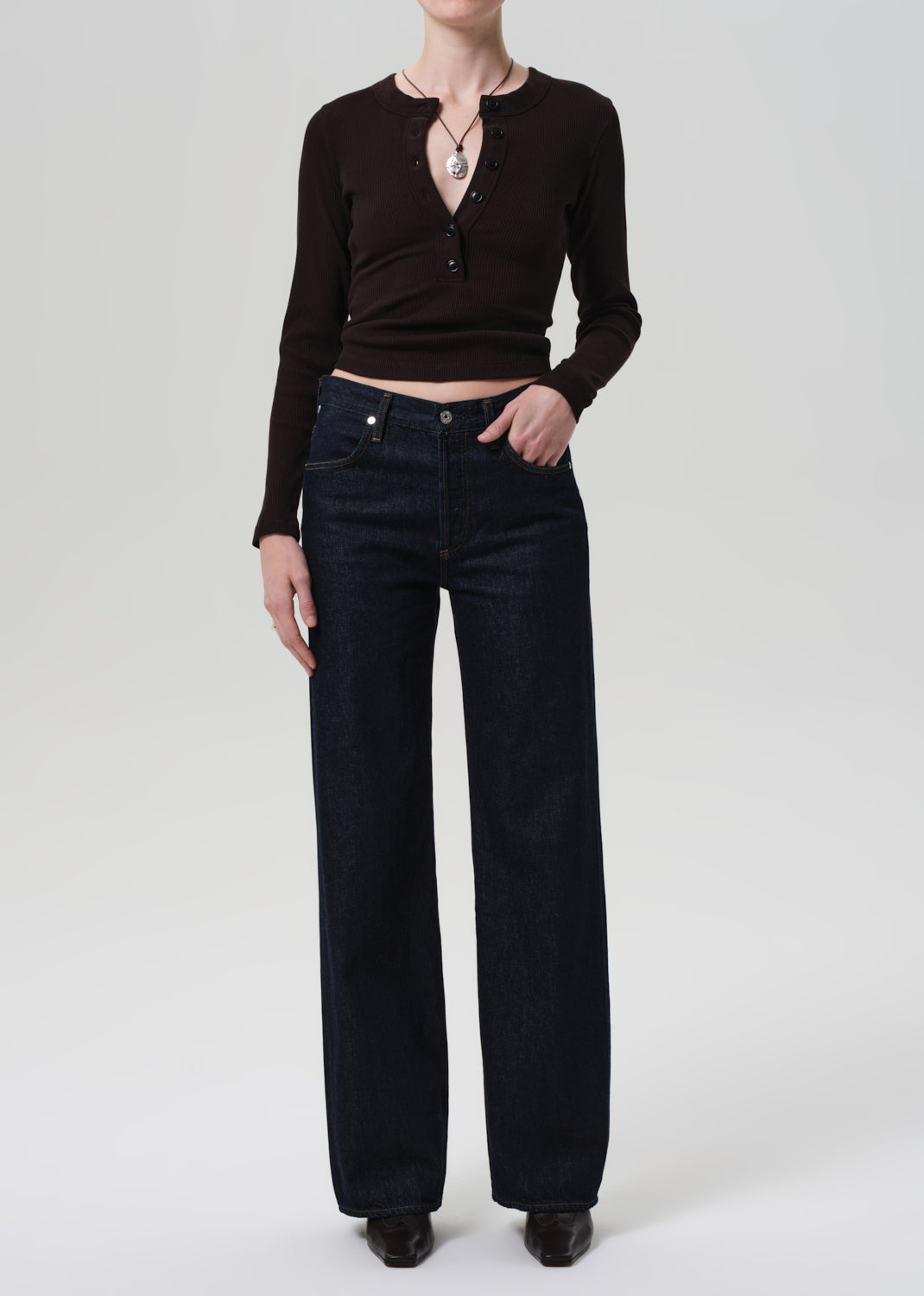 Person wearing a brown long-sleeve top and dark blue jeans on a light gray background