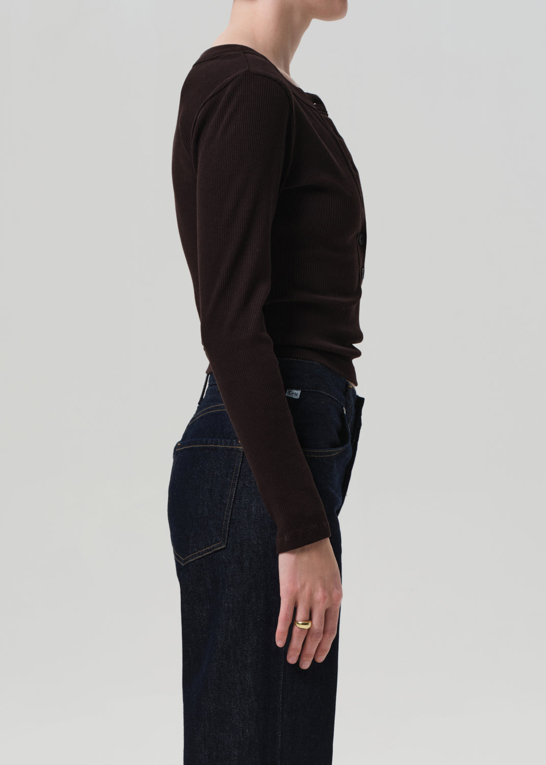 Person wearing a brown long-sleeve top and dark blue jeans on a light gray background
