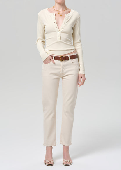 Person wearing a cream long-sleeve shirt and cream jeans with a brown belt on a gray background