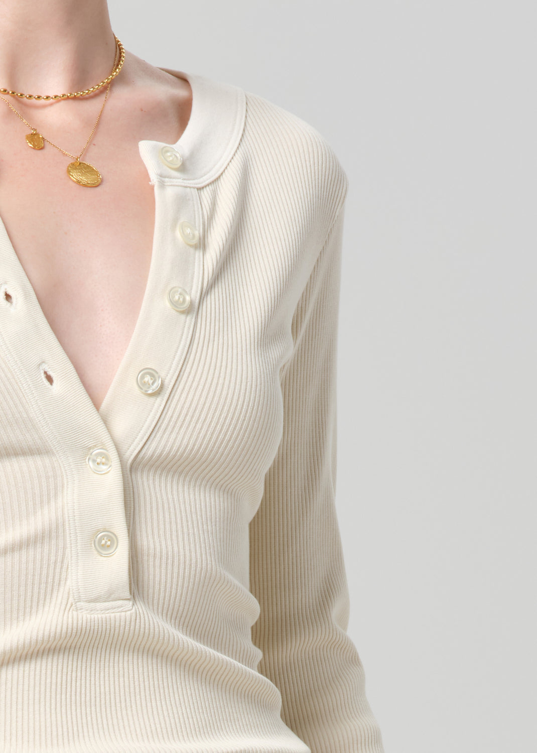 Person wearing a cream long-sleeve shirt and cream jeans with a brown belt on a gray background
