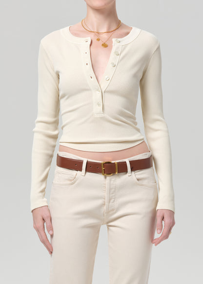 Person wearing a cream long-sleeve shirt and cream jeans with a brown belt on a gray background