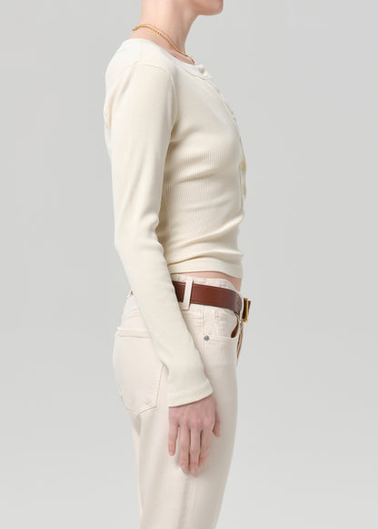 Person wearing a cream long-sleeve shirt and cream jeans with a brown belt on a gray background