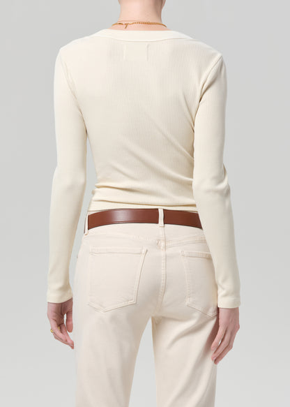 Person wearing a cream long-sleeve shirt and cream jeans with a brown belt on a gray background