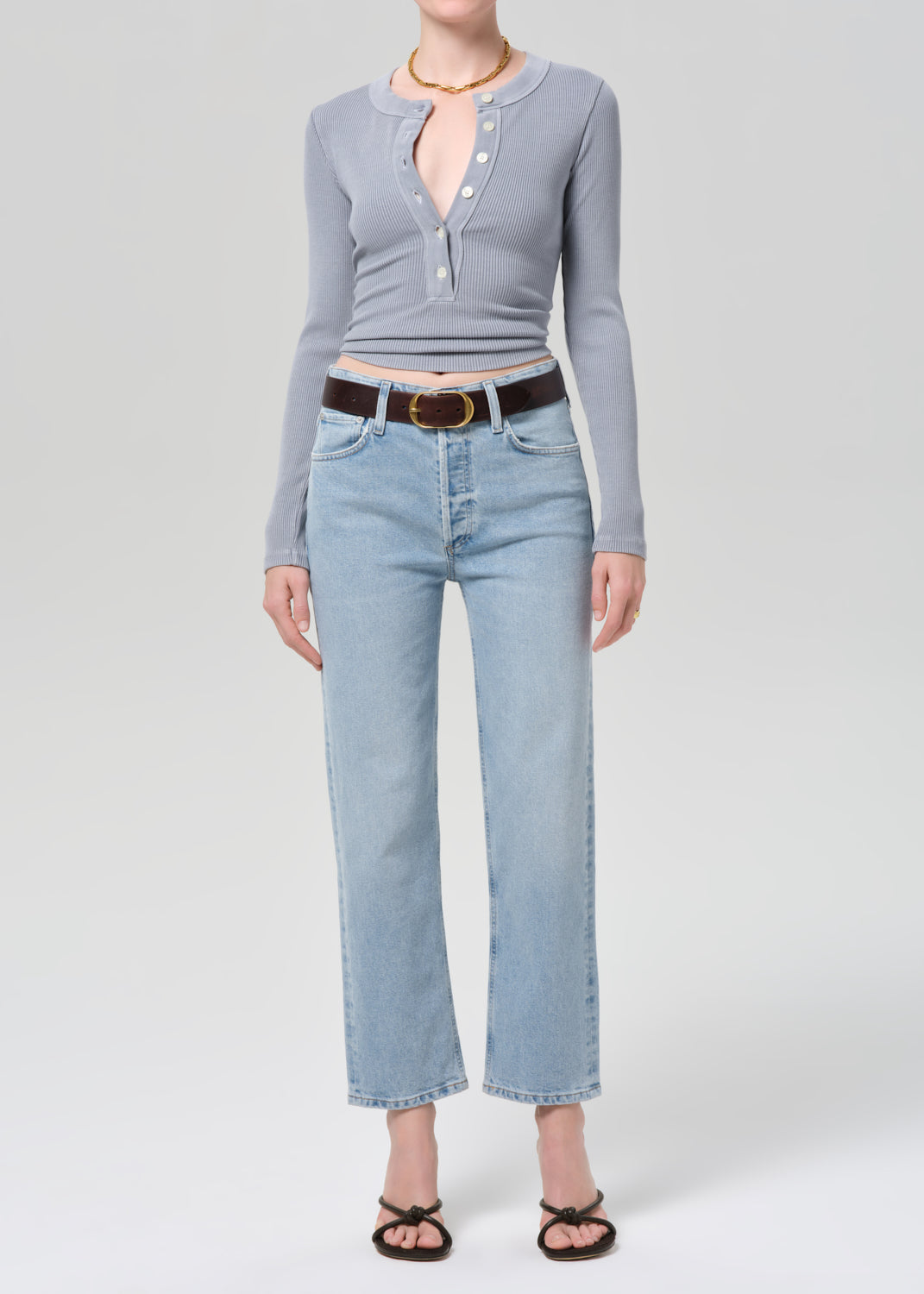 Person wearing a gray long-sleeve top and light blue jeans on a white background