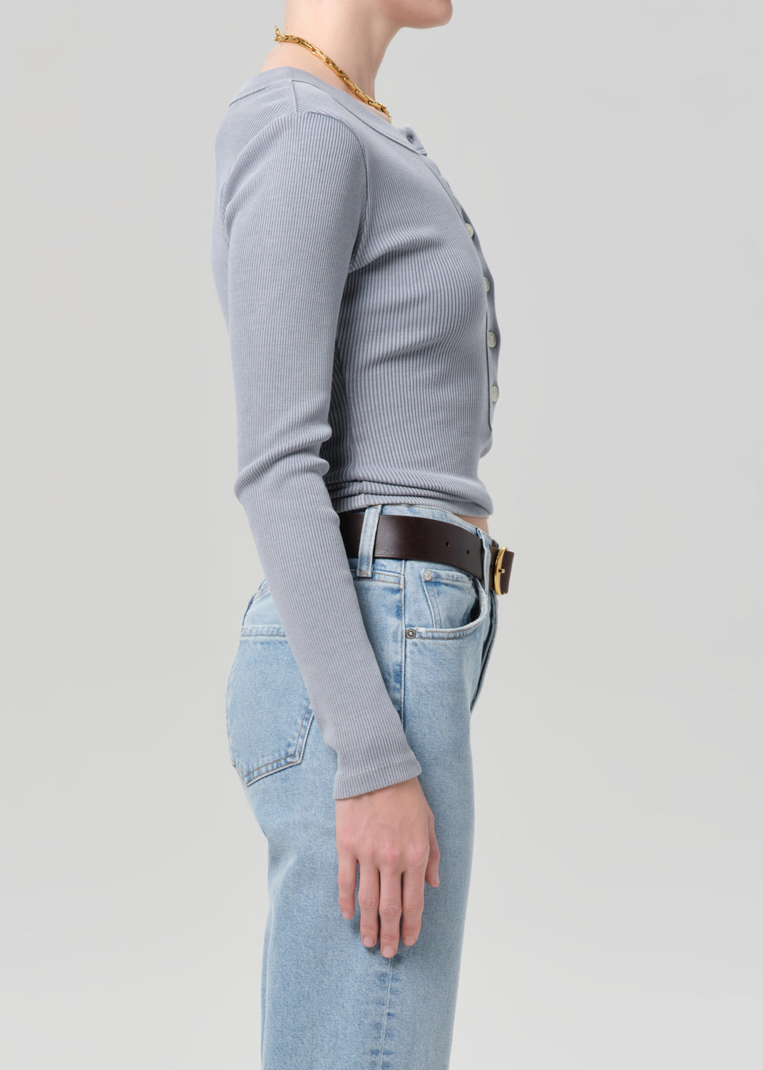 Person wearing a gray long-sleeve shirt and light blue jeans on a plain background