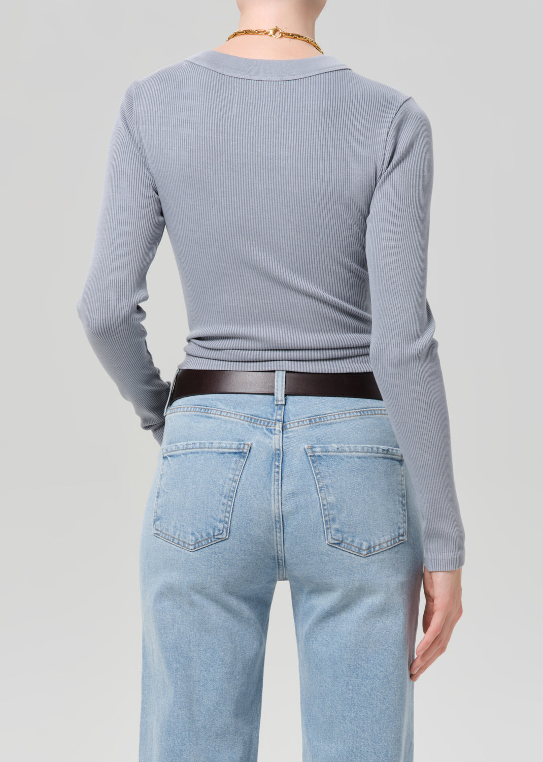 Person wearing a light gray long-sleeve top and light blue jeans on a plain background