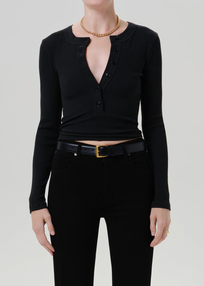 Person wearing a black long sleeve henley top with black pants on a grey background